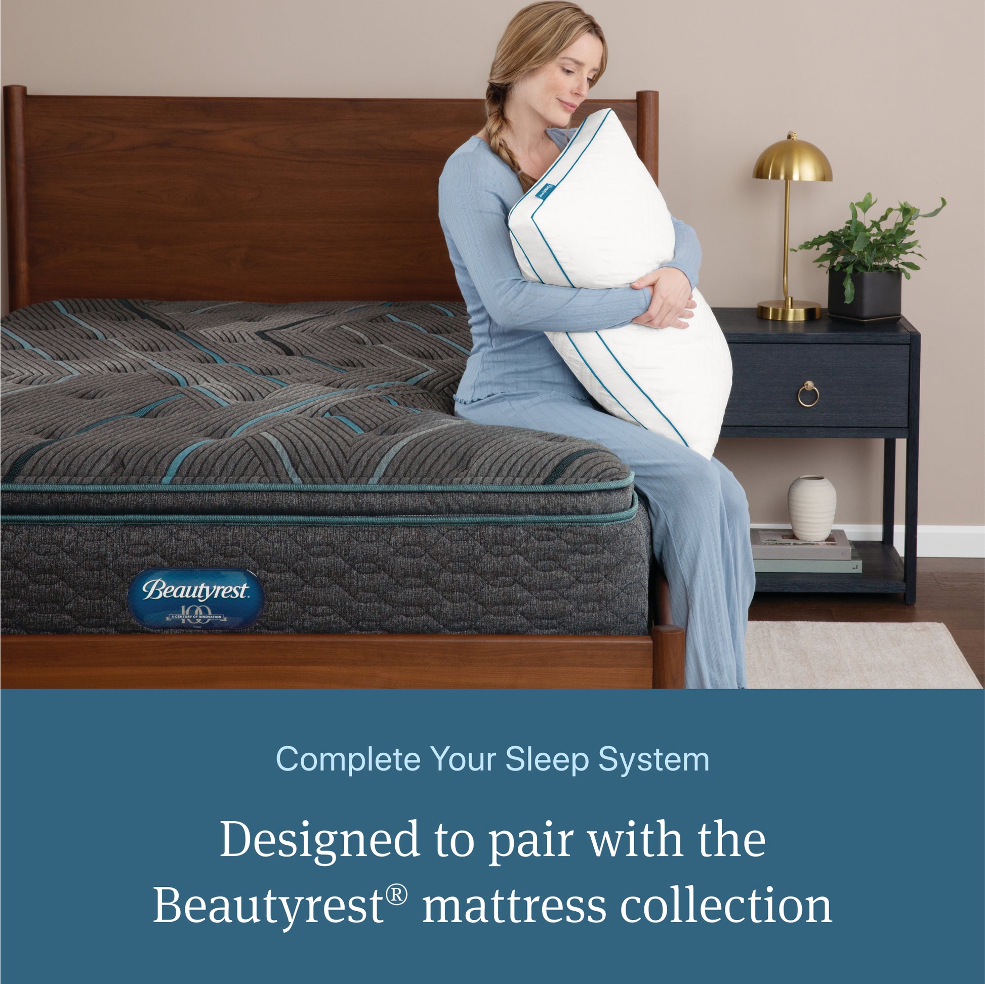 Woman sitting on a Beautyrest mattress holding a Beautyrest Down Alternative Pillow