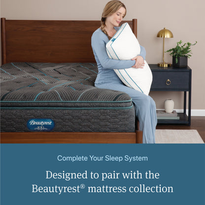 Woman sitting on a Beautyrest mattress holding a Beautyrest Down Alternative Pillow