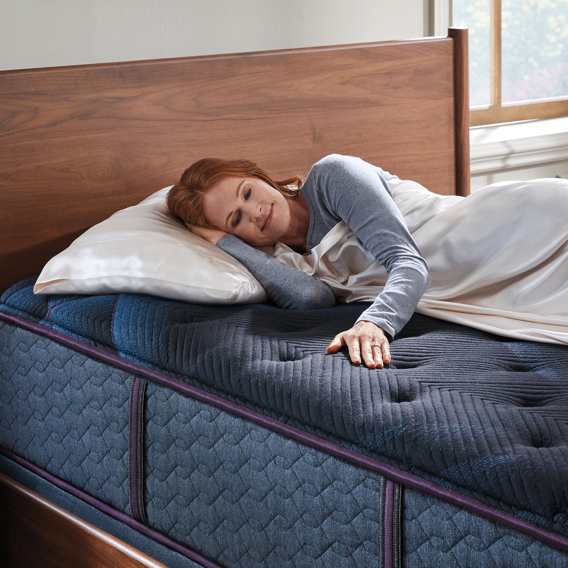 Woman laying on a World Class mattress on her right side under a blanket ribbing the mattress with her left hand.