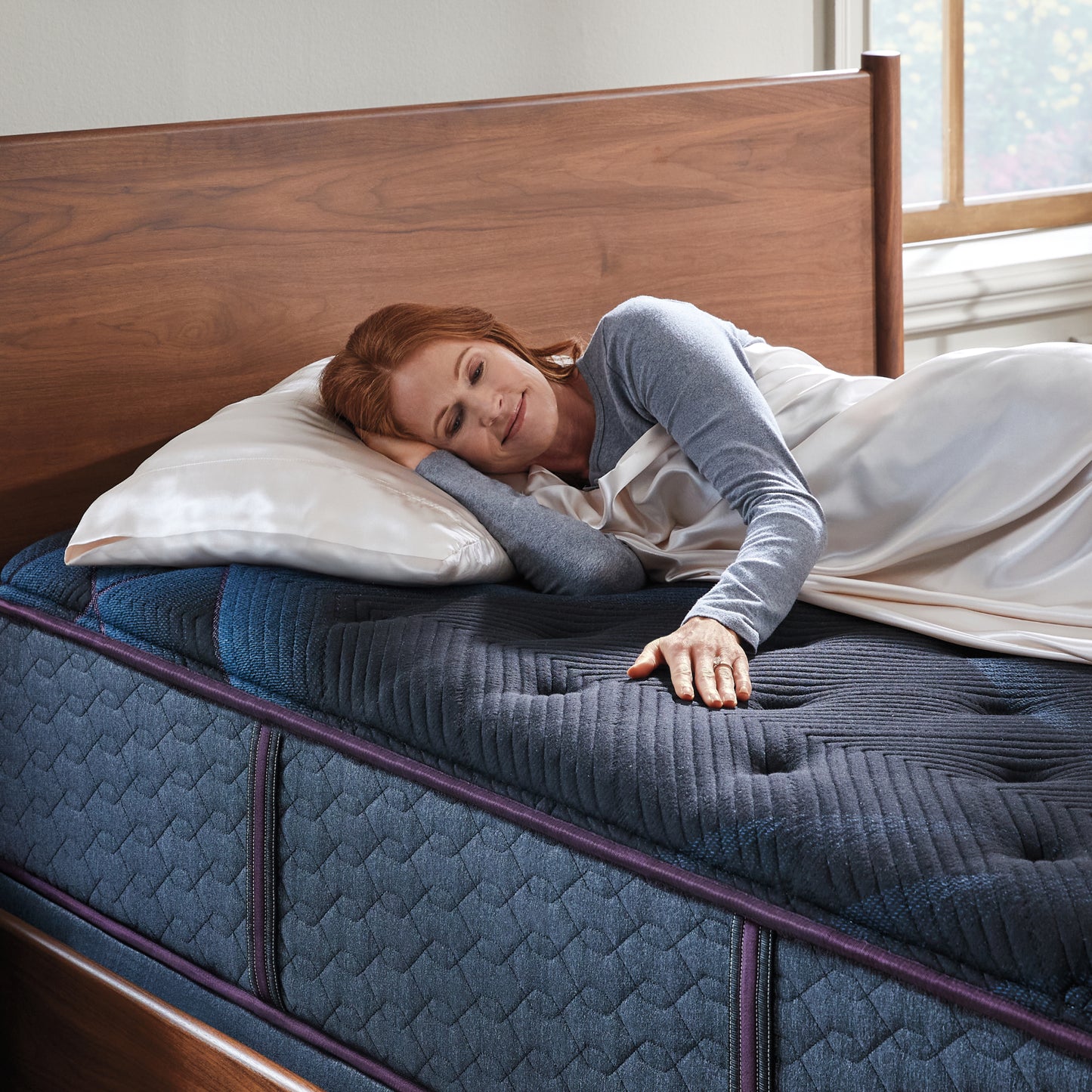 Woman laying on a World Class mattress on her right side under a blanket ribbing the mattress with her left hand.