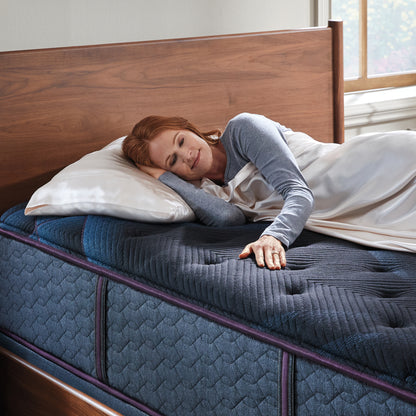 Woman laying on a World Class mattress on her right side under a blanket ribbing the mattress with her left hand.
