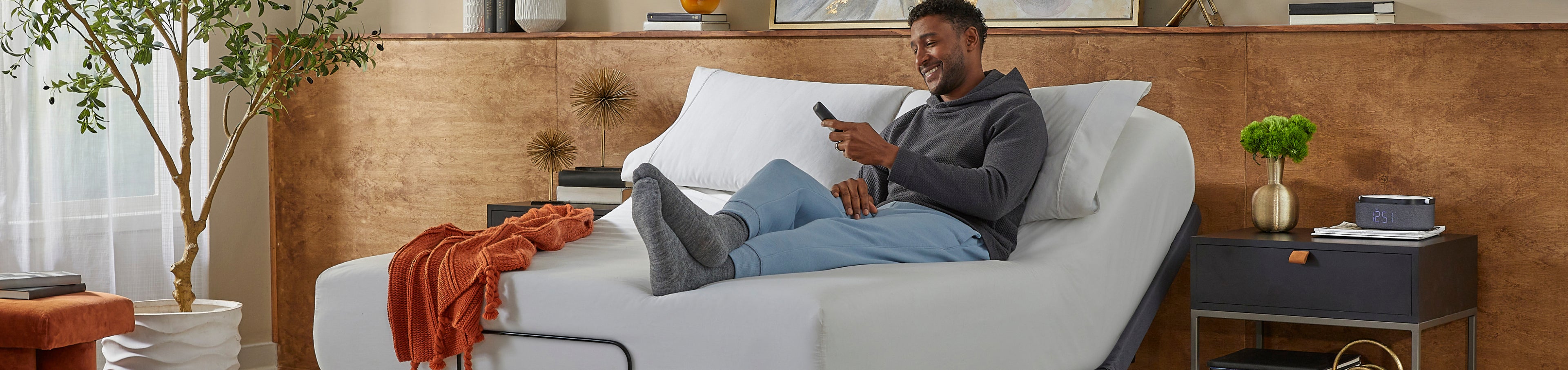 Man sitting on a white mattress on a baslogic gold base holding a remote