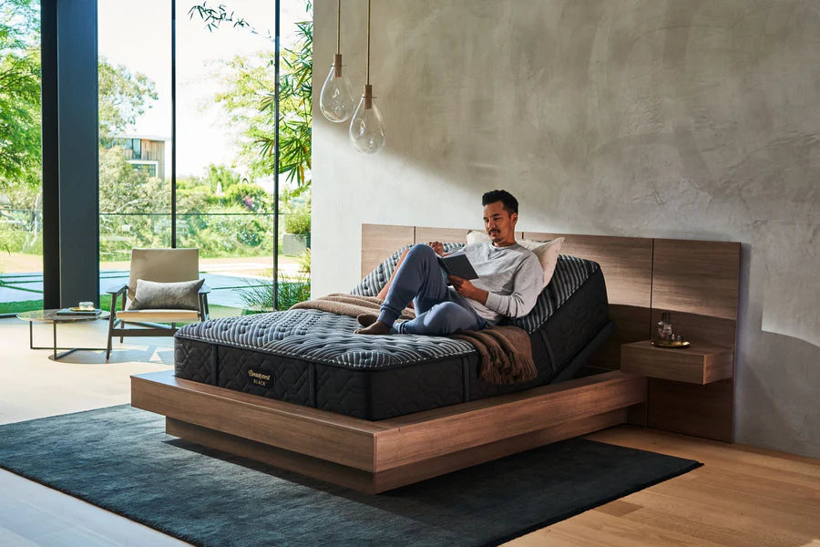 A man easily reading his book by using the head prop functionality of a Beautyrest adjustable bed frame.