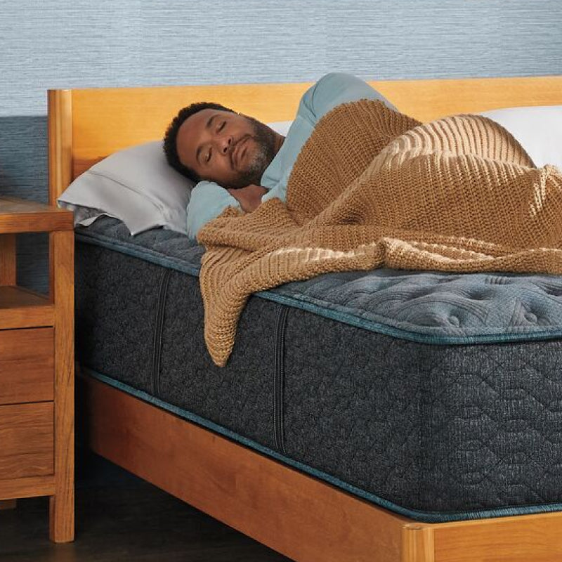 Man laying on a Beautyrest mattress on his right side asleep with a brown blanket on
